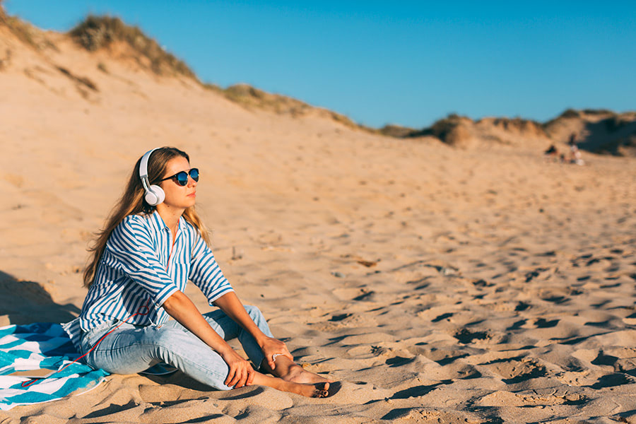 Woman sitting near a beach dune in Aveiro, Portugal, reflecting the serene lifestyle attracting Quick Home Sales.